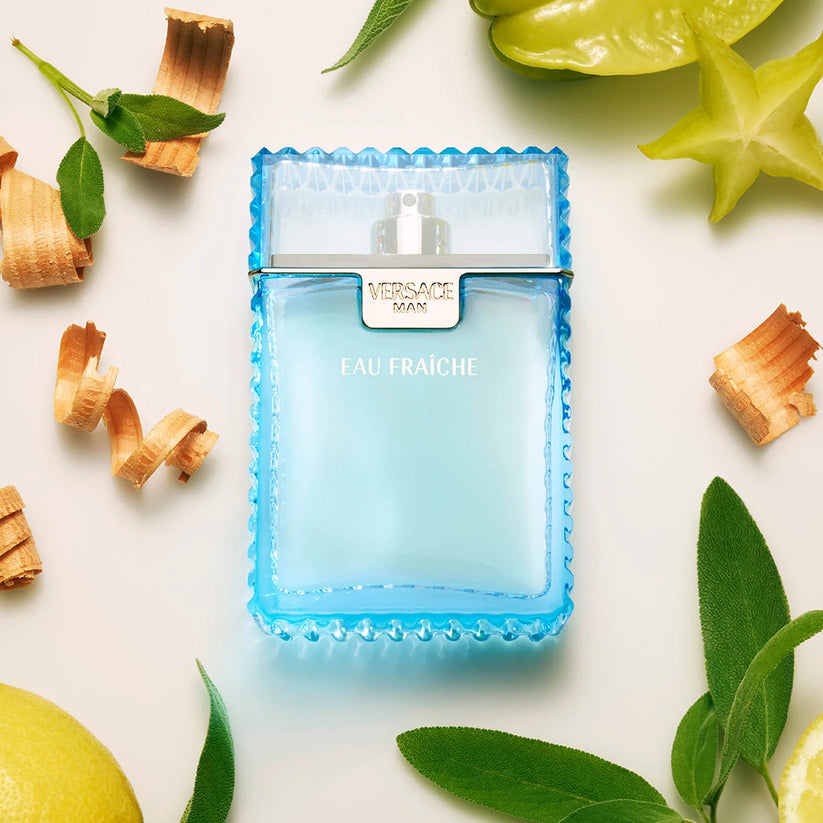 Blue Versace Man Eau Fraçèche perfume bottle surrounded by leaves and fruits on a light background