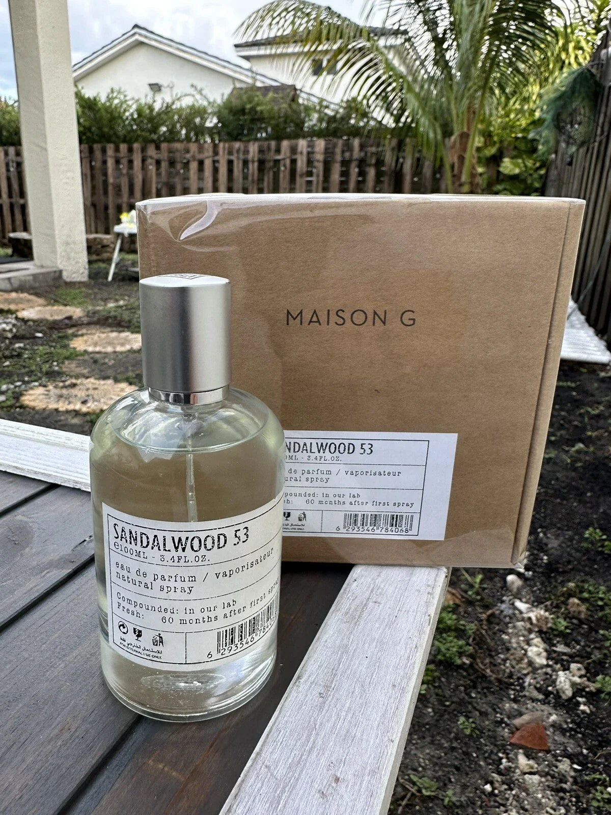 Bottle of Sandalwood 53 perfume by Maison G on a wooden surface with a cardboard box in the background.