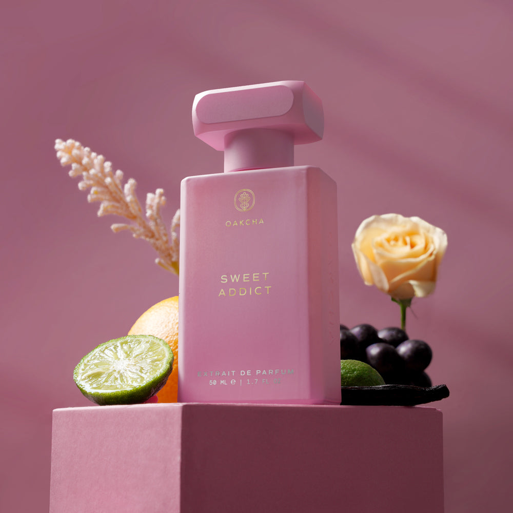 Pink perfume bottle labeled 'Sweet Addict' with floral and fruit elements on a pink background