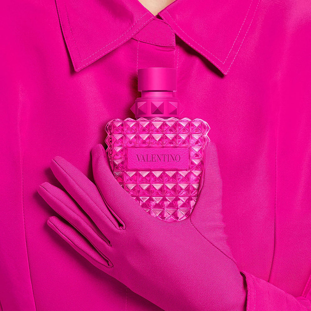 Pink textured bottle held by a hand against a pink background