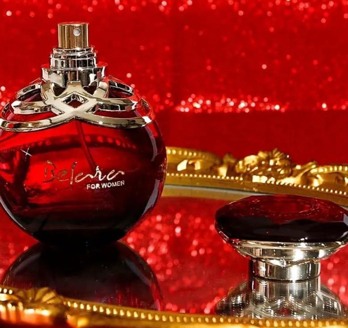Red perfume bottle with gold cap on a reflective surface against a red glittery background